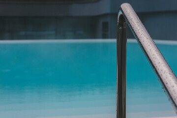 A close-up shot captures the water droplets on a polished handrail next to the clear pool water. The scene showcases a refreshing, modern design.