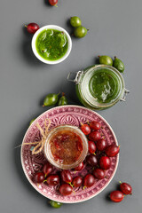 Jars and bowl with tasty gooseberry jam on grey background