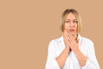 Beautiful mature woman suffering from toothache on brown background