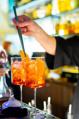 A bartender prepares Aperol Spritz cocktails with orange slices, creating a vibrant and refreshing scene at a bar. The bright colors contrast with ice cubes, enhancing the visual appeal.