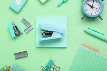 Modern school supplies with stapler on green background