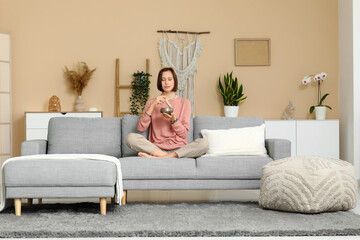 Young woman with Tibetan singing bowl meditating while sitting on sofa at home