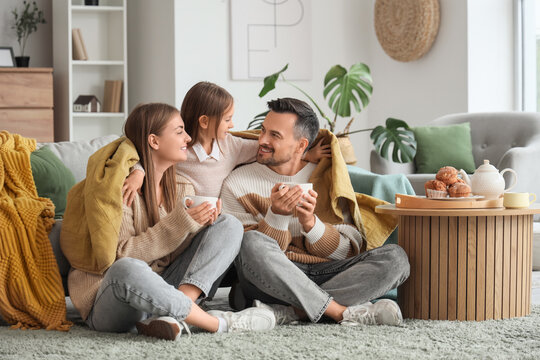 Little girl hugging her parents with warm plaid and cups of tea at home
