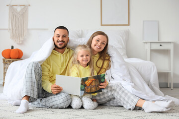 Happy parents with their little daughter reading book under blanket in bedroom