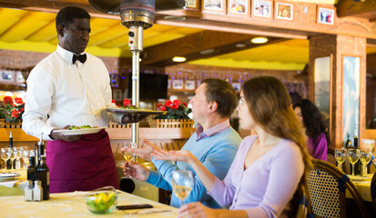 Caucasian man and woman quarreling with African-american man waiter in restaurant.