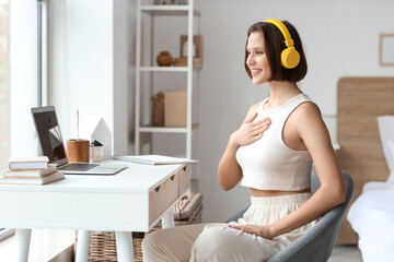 Beautiful young woman with headphones and laptop meditating in bedroom