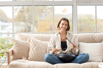 Meditating young woman playing glucophone on sofa at home