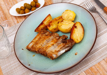 Roasted juicy pork ribs with fried potatoes served on plate.