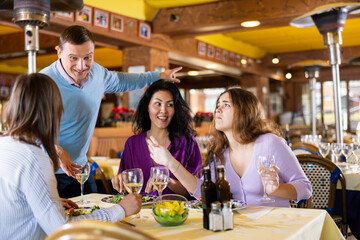 Man having conversation with women who sitting at table and dining in restaurant.