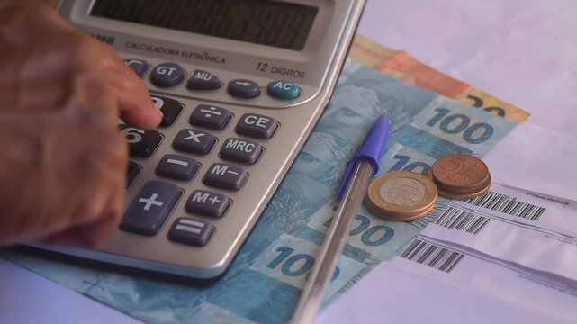 Man hand typing on calculator button to calculate for personal tax or expense budget on the wooden table inside of the house with blurred paper note and bills. Financial and money saving concept