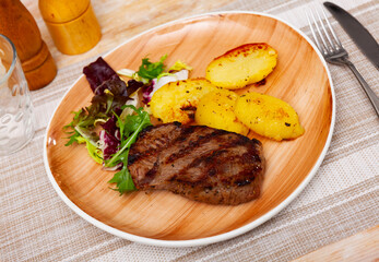 Delicious grilled beef steak served with vegetable garnish of baked potatoes and fresh greens..