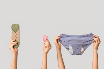 Female hands with period panties, reusable pad and menstrual cup on grey background