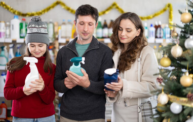 Couple adult man and woman with daughter chooses cleaning spray in household chemicals store decorated for christmas