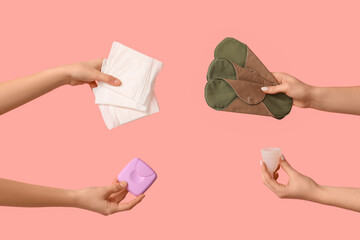 Female hands with menstrual cup, tampons storage box and reusable pads on pink background