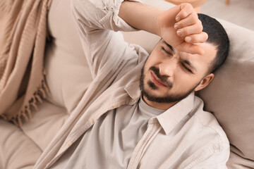 Young man feeling unwell on sofa at home, closeup