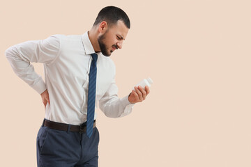 Young businessman with pill bottle suffering from back pain on light background