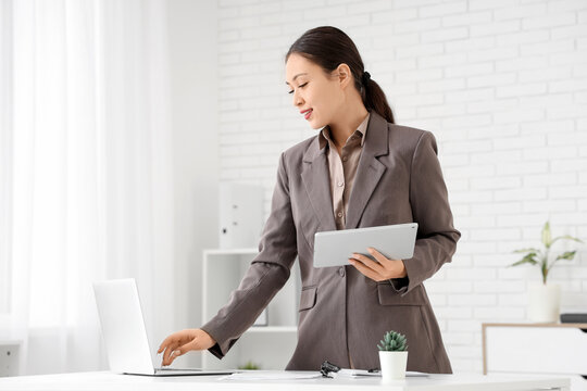 Young Asian businesswoman with laptop and tablet computer working at her workspace in office