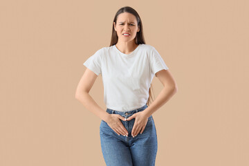 Young woman suffering from menstrual cramps on beige  background