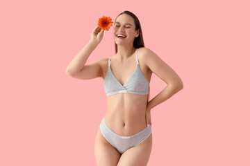 Young woman in underwear and with flower on pink background