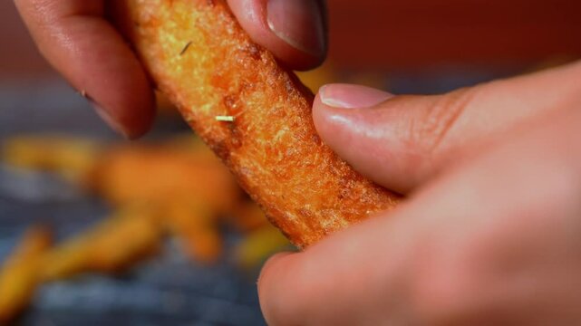 Hands breaking up crispy yuca with French fries in the background