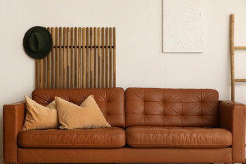 Brown leather sofa with soft pillows near white wall in living room