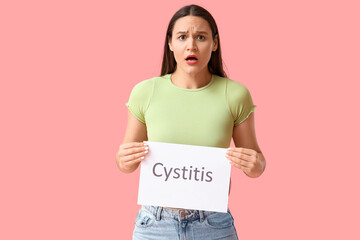 Young woman holding paper with word CYSTITIS on pink background