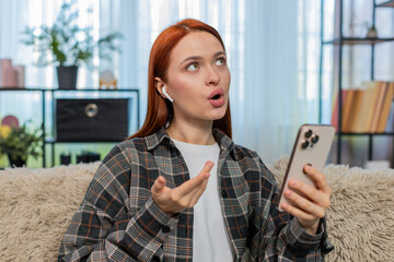 Young woman at home learning new language using mobile app and repeating words aloud with focus and...