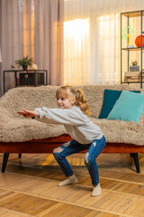 Healthy teenager girl stands at home performing simple squats and counting one, two, three with...