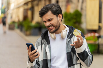 Shocked Hispanic man trying to pay online shopping with smartphone blocked credit card. Annoyed...