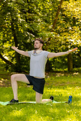 Athletic sporty fit man doing workout yoga breathing exercise on sports mat in park. Raising hands....