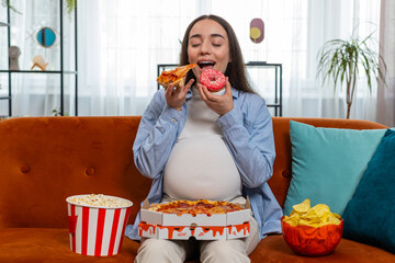 Pregnant woman eating unhealthy junk food pizza popcorn crisp sitting on couch in home living room. Fast fatty food during pregnancy in apartment. Hunger, change in taste preferences. Expecting baby