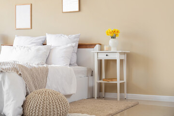 Interior of stylish bedroom with cozy bed and beautiful narcissus flowers on bedside table
