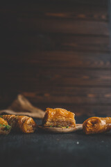 Close-up of traditional baklava pieces with layered golden pastry and syrup on dark rustic background. Sweet dessert with flaky texture and pistachio crumbs