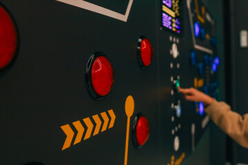 Child’s hand pressing a glowing red button on an interactive control panel with multiple lights, in a modern science or technology exhibit