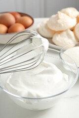 Whisk with whipped cream and other ingredients on light table, closeup. Cooking meringue cookies