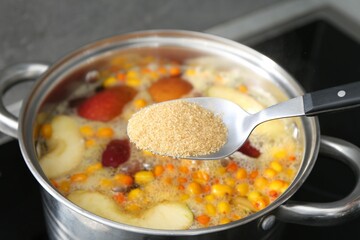 Adding sugar into tasty compot in pot on stove, closeup