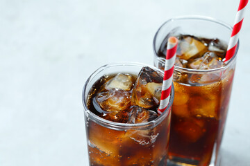 Refreshing cola with ice cubes and straws in glasses on light table, closeup. Space for text