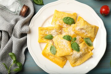 Delicious ravioli with cheese and basil served on light blue wooden table, flat lay
