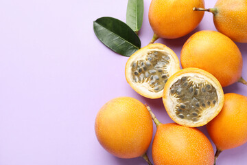Ripe yellow passion fruits and leaves on lilac background, flat lay. Space for text