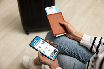 Tourist holding mobile phone with e-ticket for bus and passport indoors, closeup