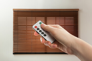 Woman using remote to control blinds in room, closeup