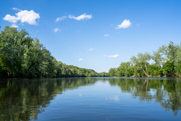 Fototapeta premium In the Middle of a Calm James River with the Reflection of the Sky and Trees Lining the Riverbank