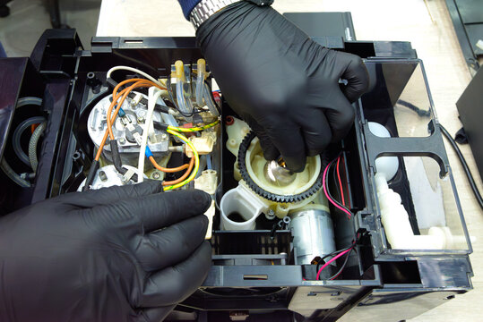 Technician adjusting gear mechanism inside coffee machine during maintenance; visible wiring, motor, and internal heating system.