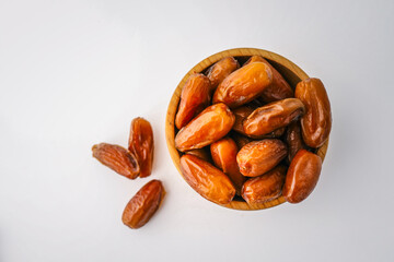 Whole dates in a round wooden bowl with some scattered around, placed on a clean white background. Minimalist, healthy food concept with natural dried fruit
