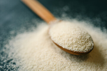 Close-up of semolina in a wooden spoon with a bowl in the background. Soft natural lighting enhances the fine texture and warm tones