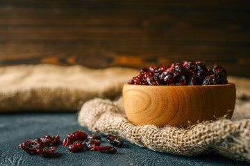 A wooden bowl of dried cranberries with some scattered on a burlap cloth and dark surface, perfect for rustic food photography or healthy snack themes