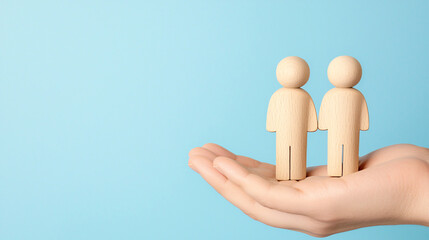 Person's hand gently holds two unpainted wooden figurines on a light blue colored background.