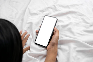 Woman lying in bed and holding smartphone in hand with blank white screen on bed