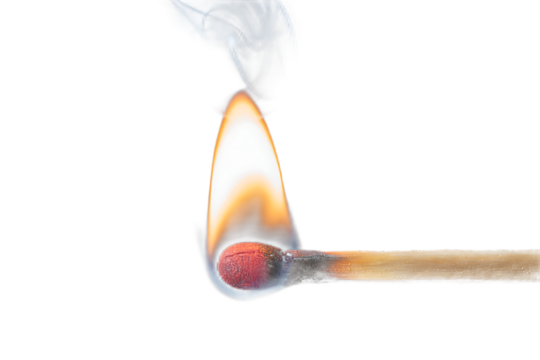 Close up of a burning match creating flame and smoke against a dramatic black background