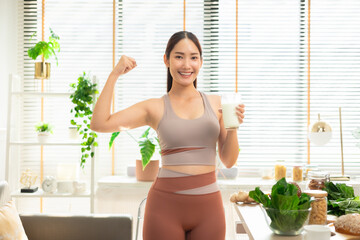 Attractive fitness asian woman finishing workout and drinking protein milk shake vitamins and vegetable after training at home. Bodybuilding. Healthy lifestyle.